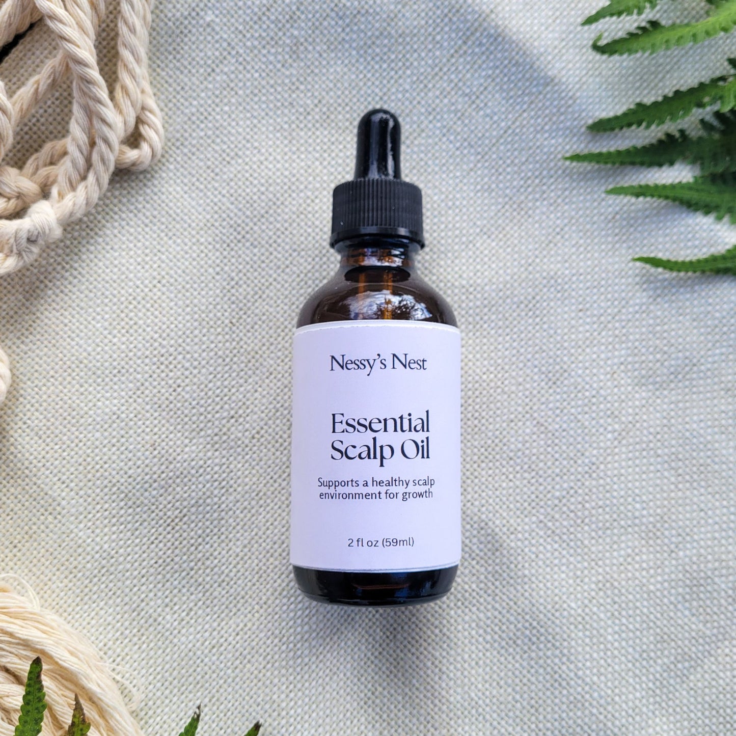 Nessy's Nest Essential Scalp Oil bottle on a textured surface with green leaves in the background.