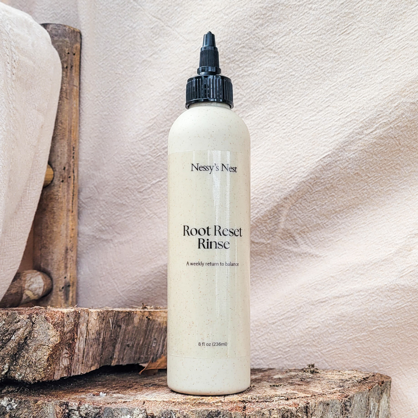 Bottle of Nessy's Nest's Root Reset Rinse on wood surface with linen beige background.