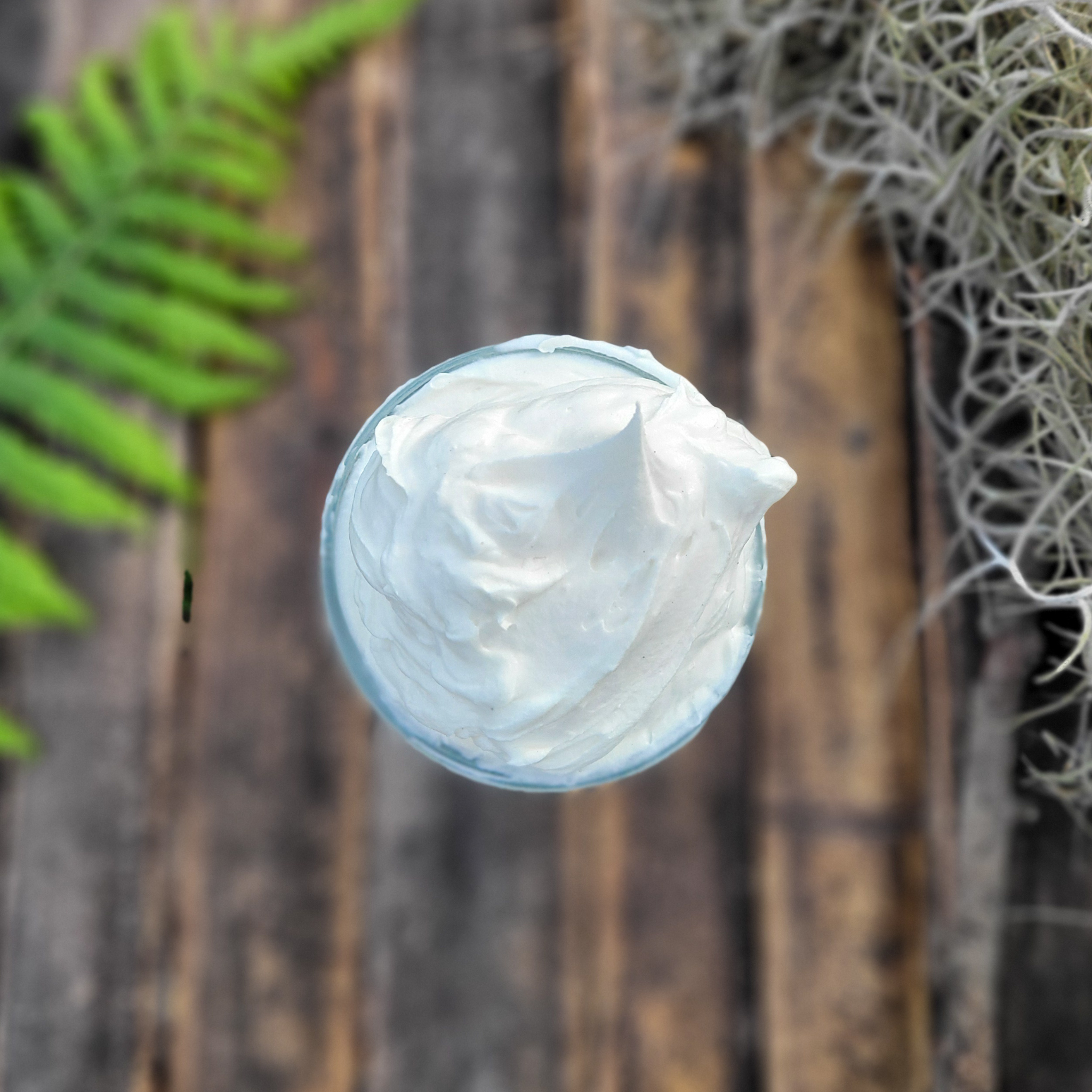Nessy's Nest Fluffy creamy top view of open jar of whipped tallow body body on wood surface background