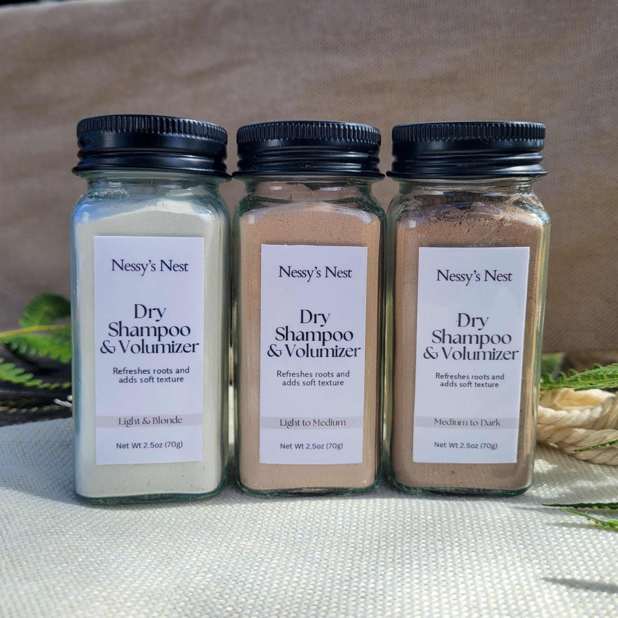 Nessy's Nest 3 jars of Dry Shampoo & Volumizer in sunlight with fabric and greenery background.
