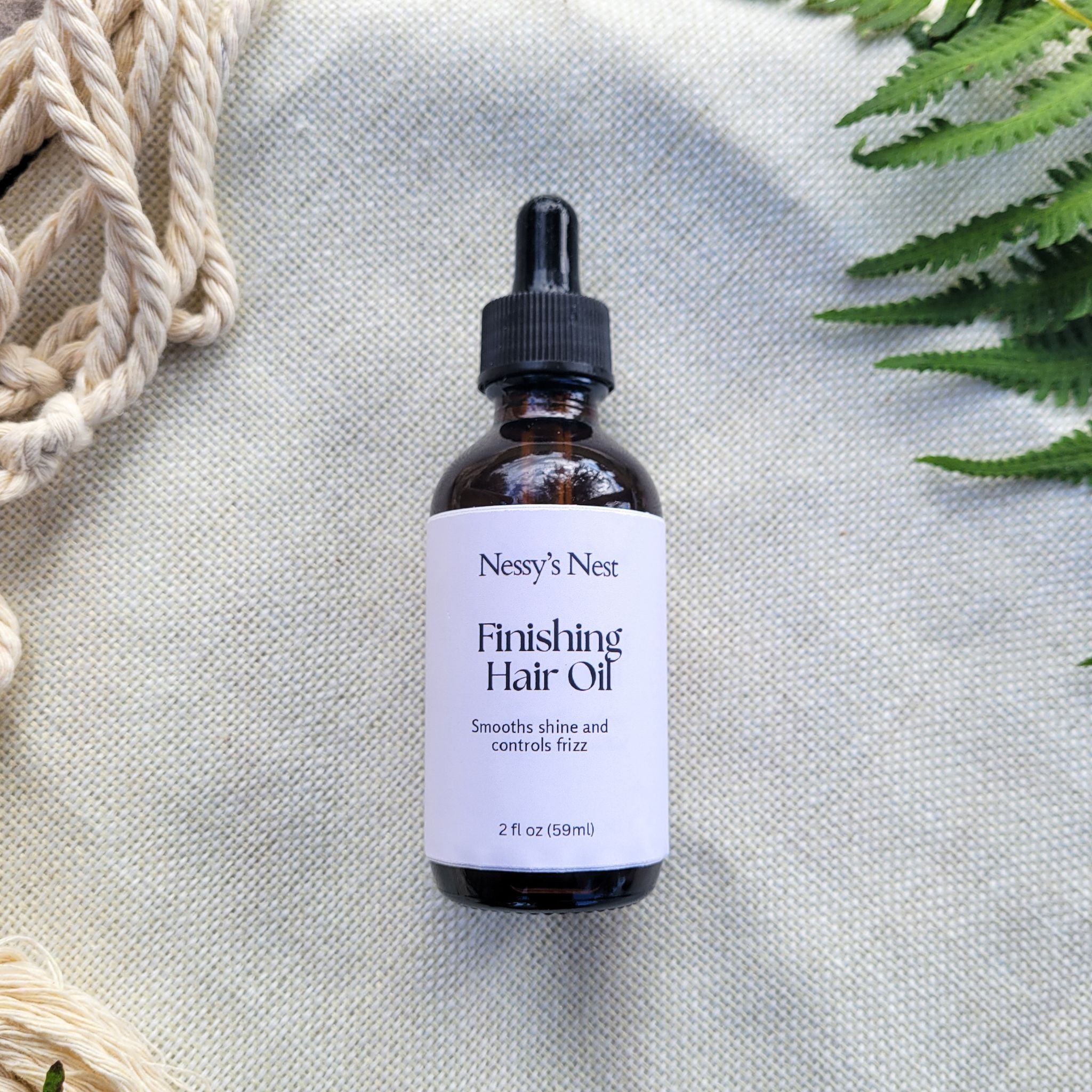 Bottle of Nessy's Nest Finishing Hair Oil on a textured surface with green leaves in the corner.