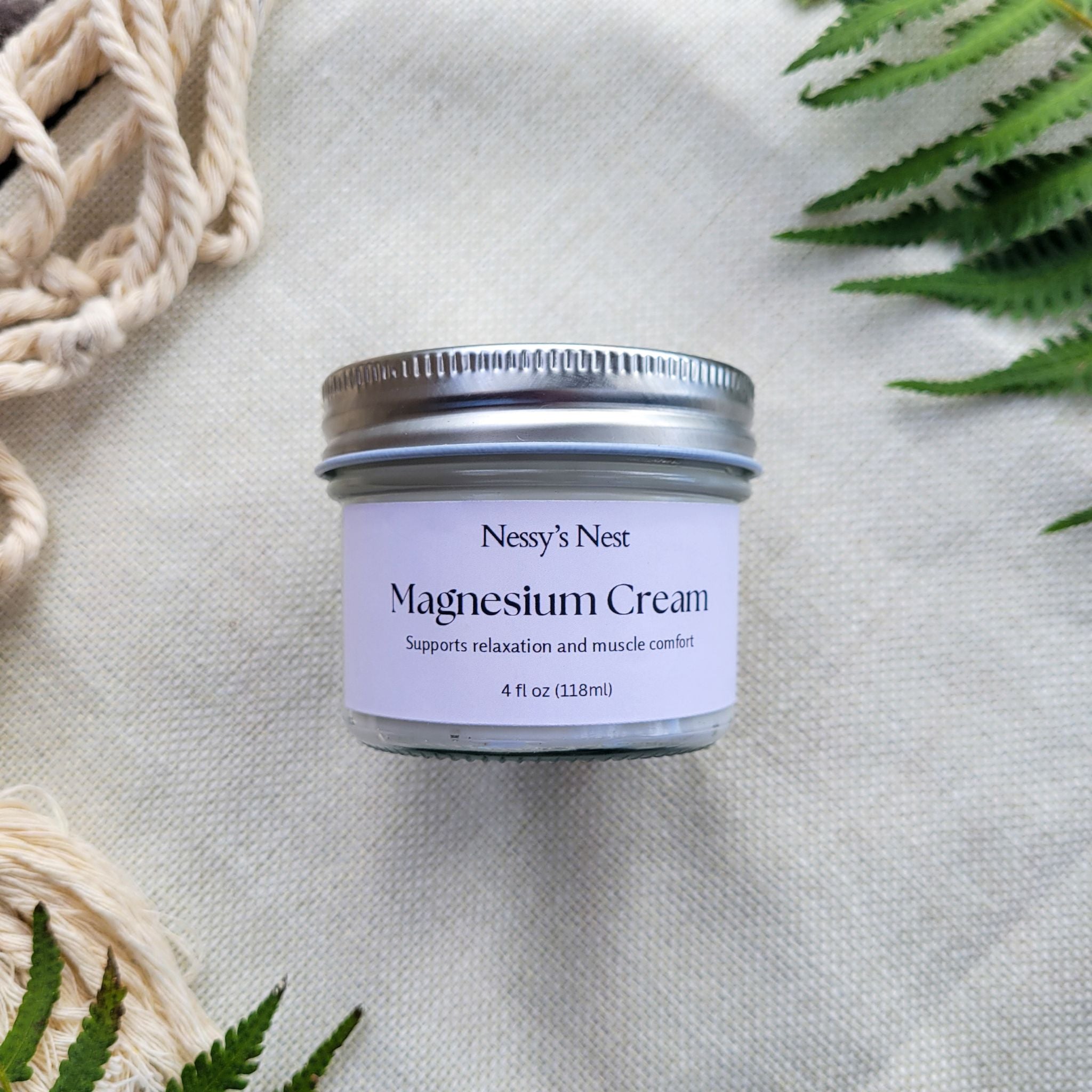 Jar of Nessy's Nest Magnesium Cream on a textured surface with plants in the background