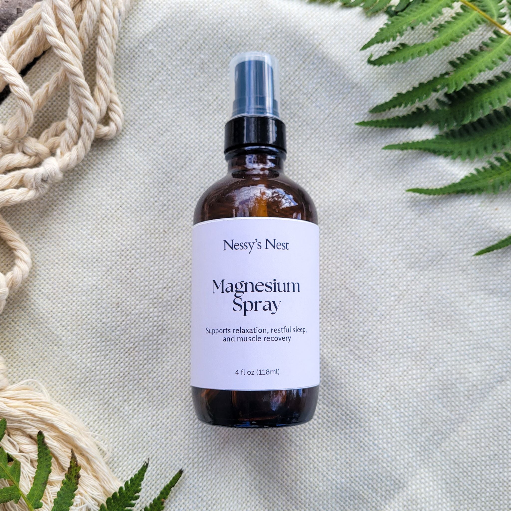Bottle of Nessy's Nest Magnesium Spray on a textured surface with green leaves.