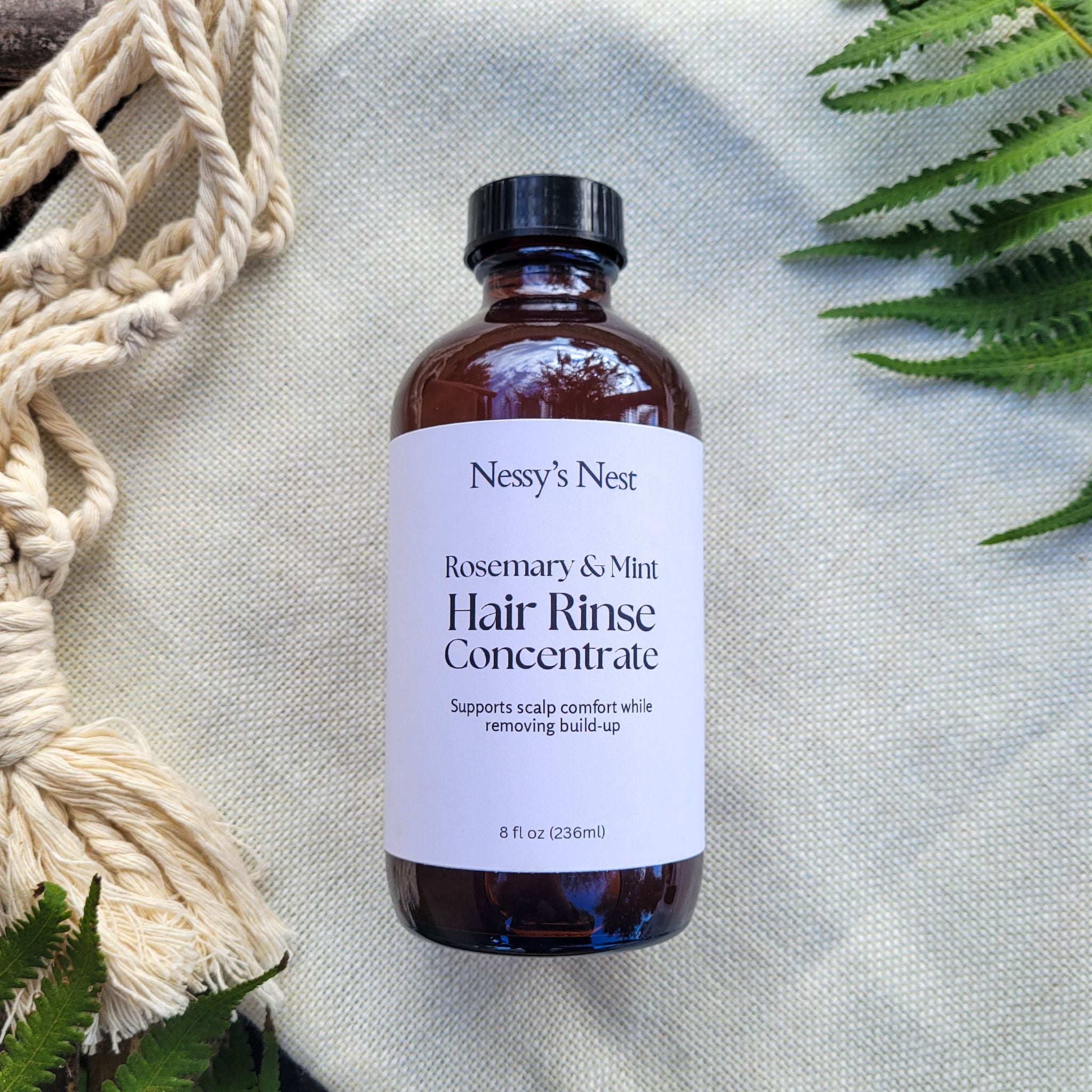 Nessy's Nest Rosemary & Mint Hair Rinse Concentrate bottle on a textured surface with greenery.