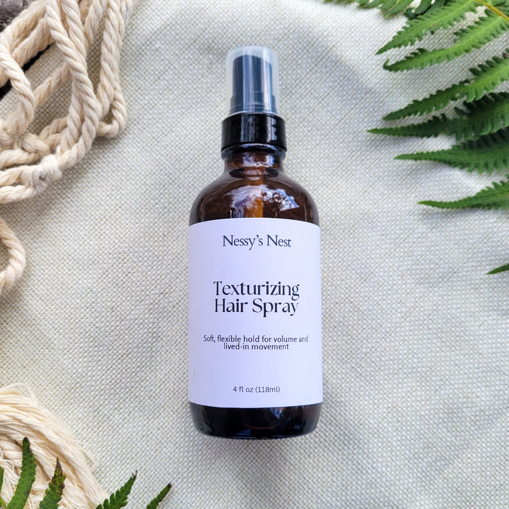 Nessy's Nest texturizing hair spray bottle on a textured surface with greenery.