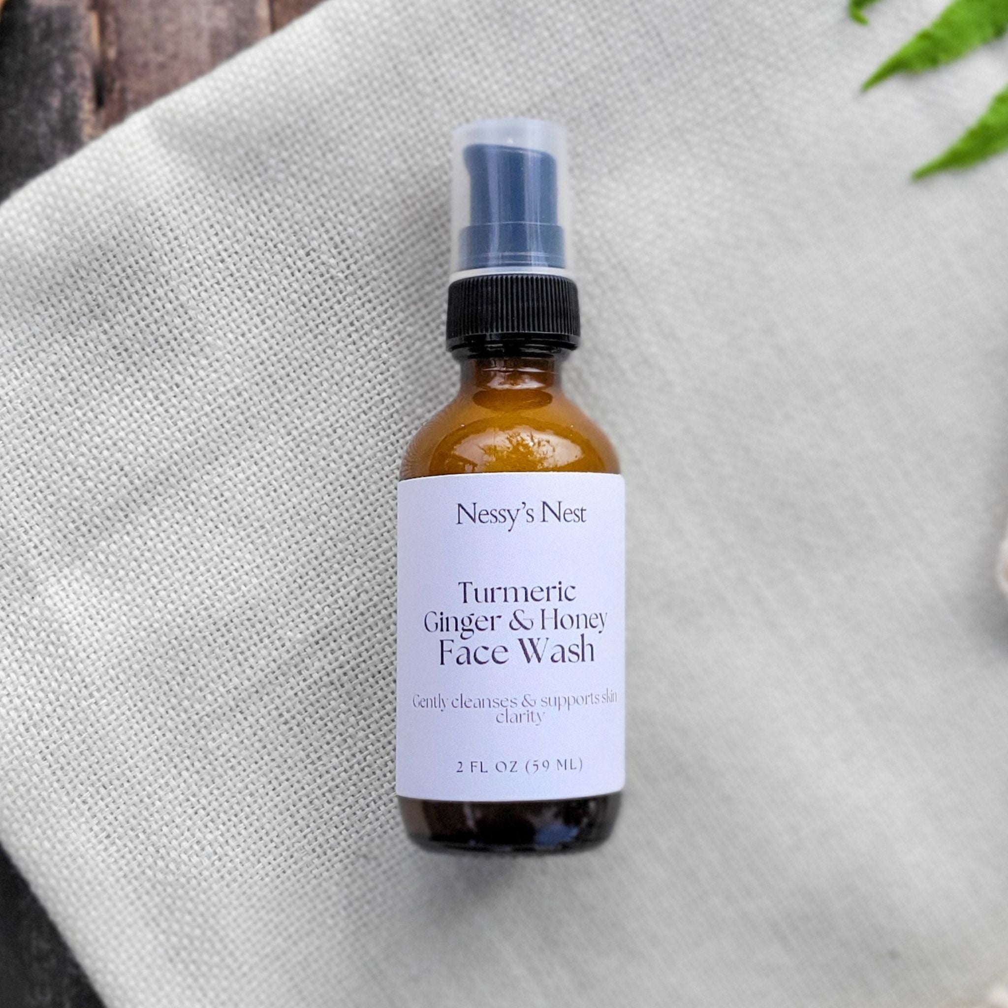 Bottle of Nessy's Nest Turmeric Ginger & Honey Face Wash on a textured surface with plants in the background
