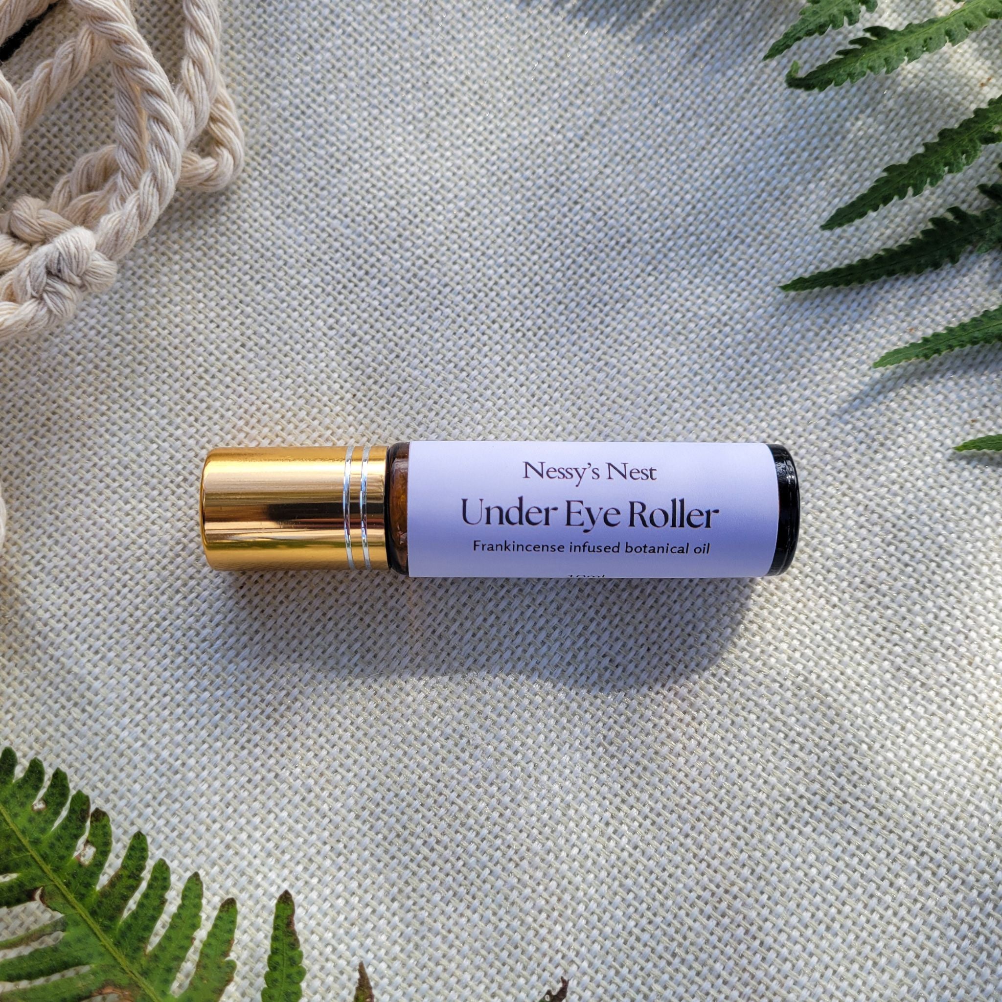 Nessy's Nest Under Eye Roller on a textured light background and greenery.