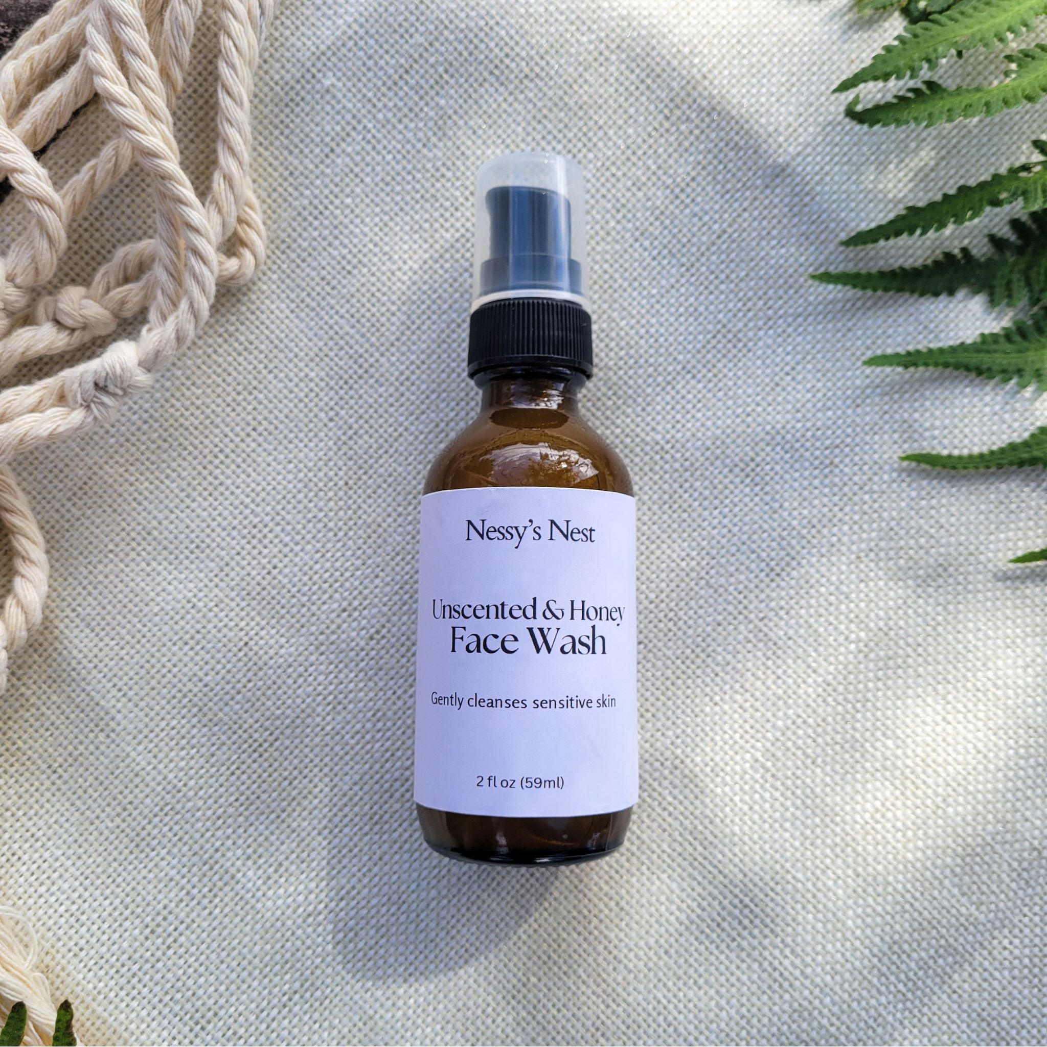 Bottle of Nesse's Nest Insected & Honey Face Wash on a textured surface with green leaves.