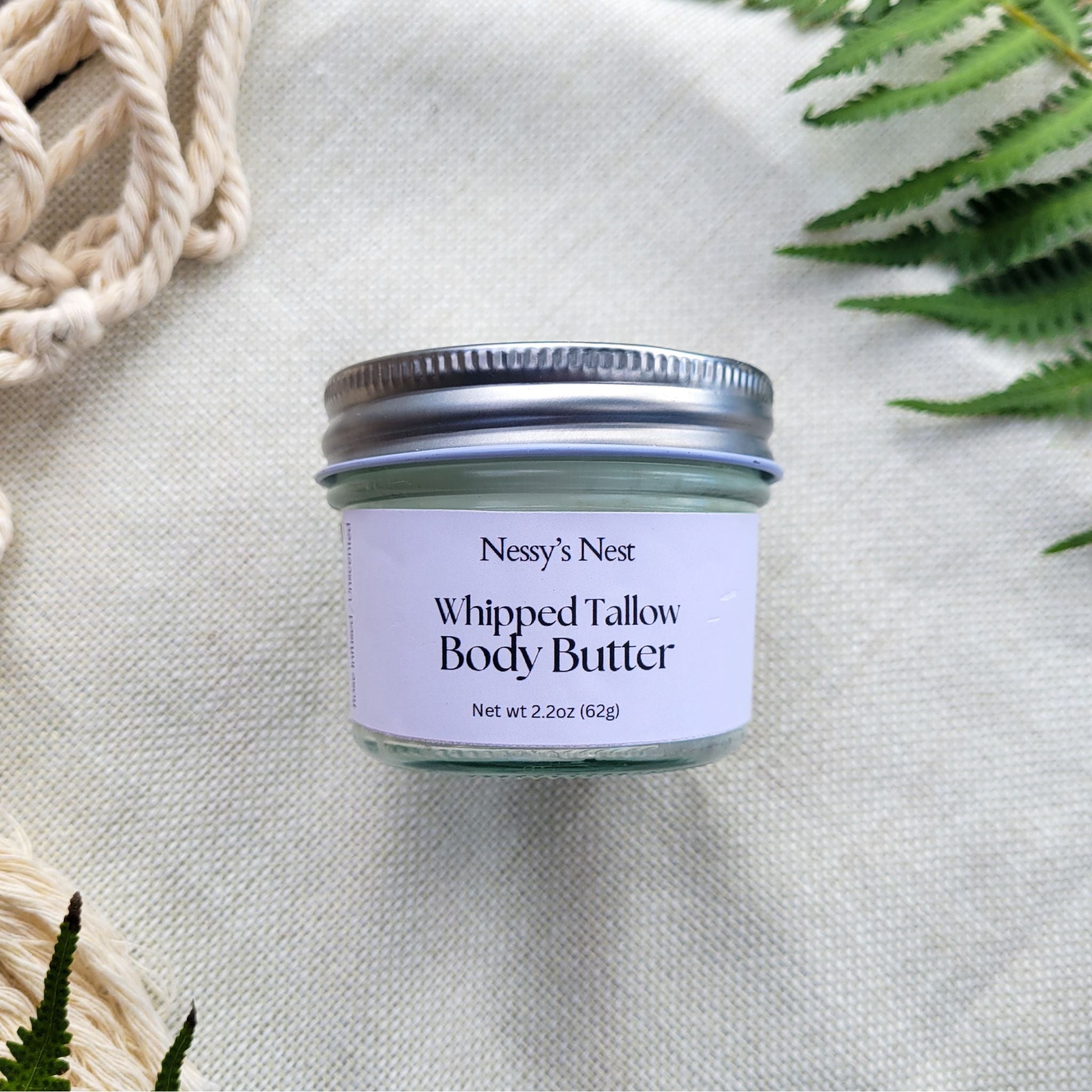 Jar of Nessy's Nest Whipped Tallow Body Butter on a textured surface with greenery.
