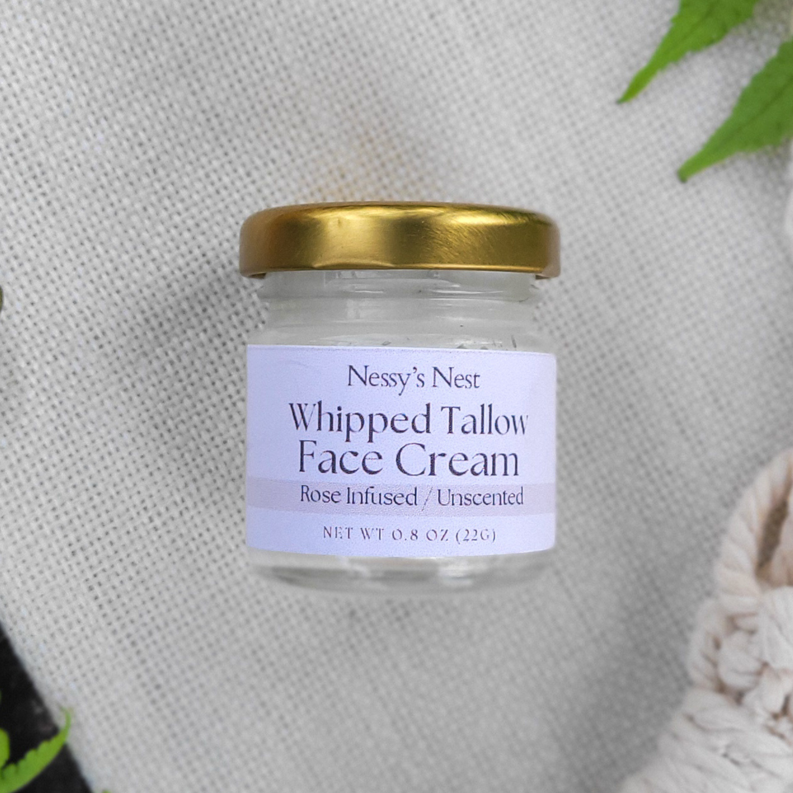 Jar of Nessy's Nest Whipped Tallow Face Cream on a textured surface with green leaves.